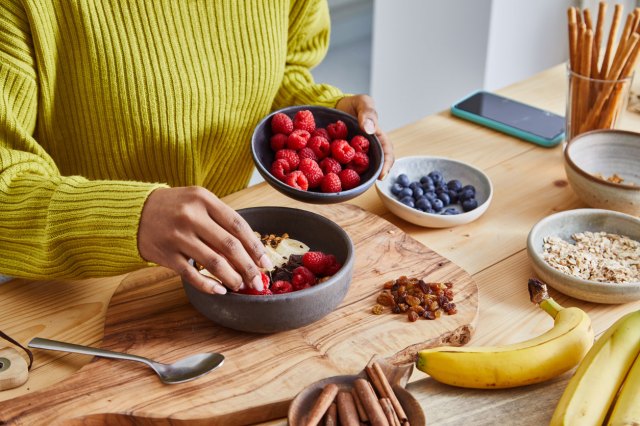 An image of a woman making a bowl of fruit, yogurt, and granola