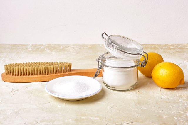 An image of citric acid, soda, lemons, and a wooden brush on a light background