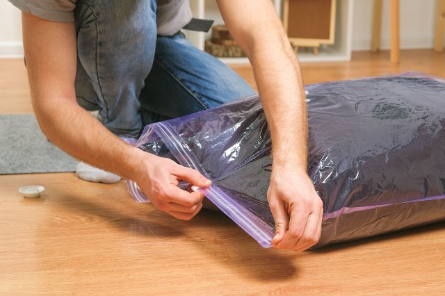 An image of a person zipping a large plastic bag with clothes in it