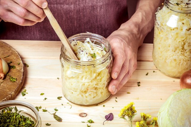 An image of a person holding wooden tongs in a jar of sauerkraut