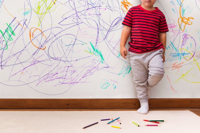 An image of a young boy standing against a wall with crayon marks