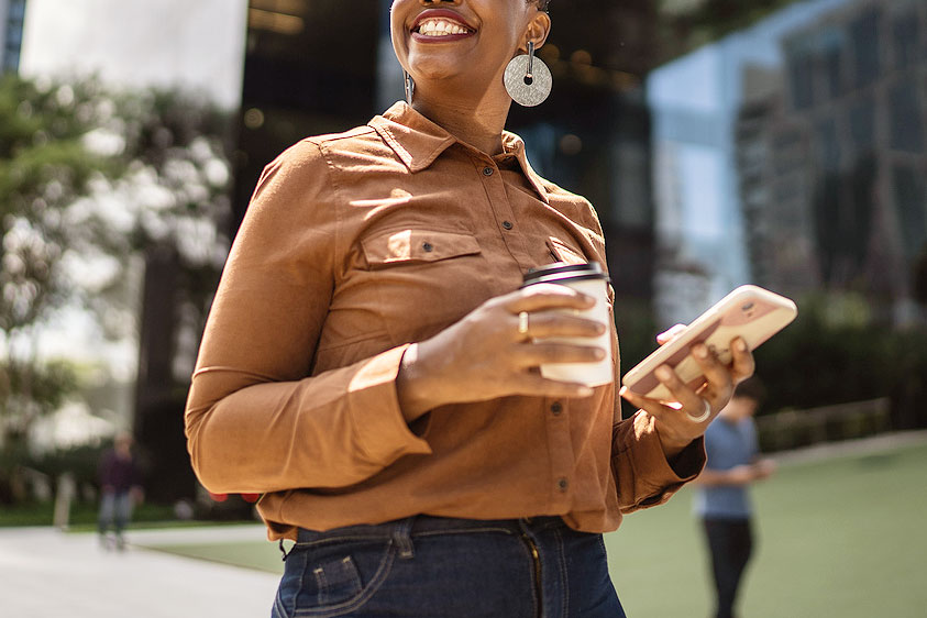 An image of a smiling woman holding a phone and a cup of cofffee