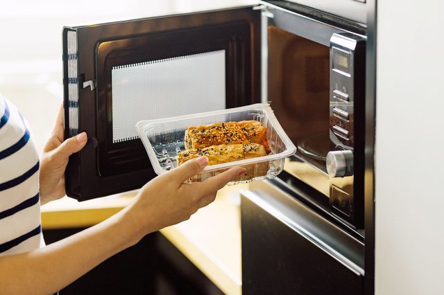 An image of a woman putting food into the microwave