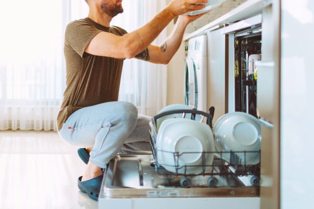 An image of a man squatting by an open dishwasher