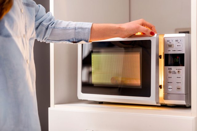 An image of a woman opening a microwave