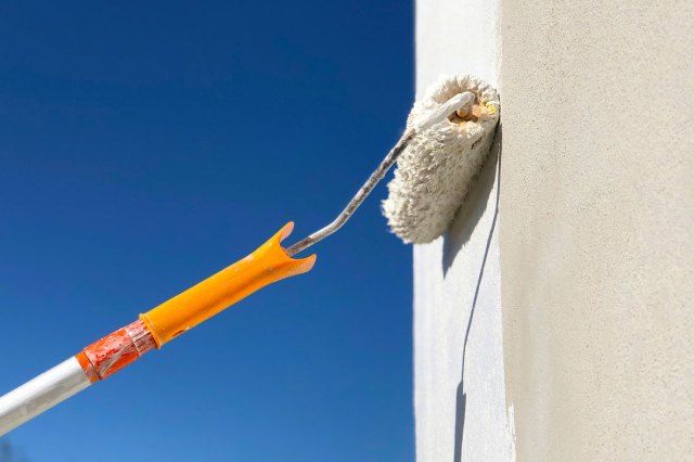 An image of a paint roller painting a building white