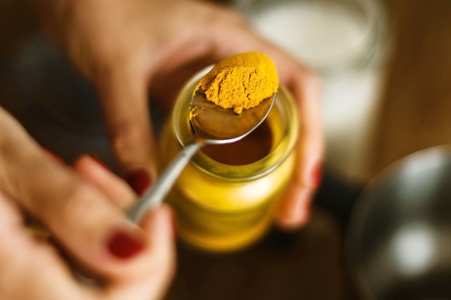 An image of someone spooning turmeric out of a jar