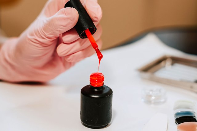 An image of a person pulling the wand out of a bottle of red nail polish