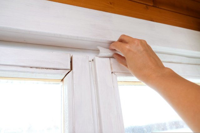 An image of a hand adding white insulation to the top of a window