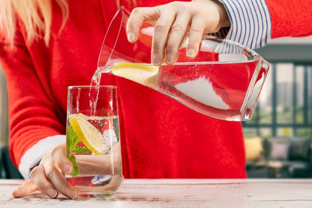 An image of a woman in a red shirt pouring a glass of water from a pitcher