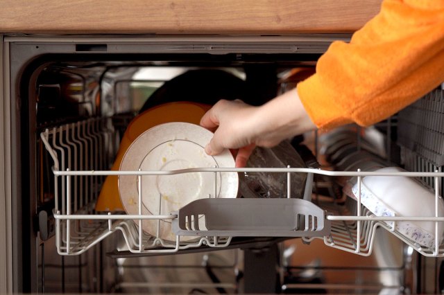 An image of a person putting a dirty dish in the dishwasher
