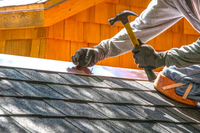 An image of a man hamming nails onto a roof