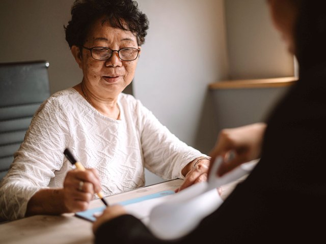 An image of an older woman signing a documen