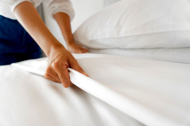 An image of a person making a bed with white sheets