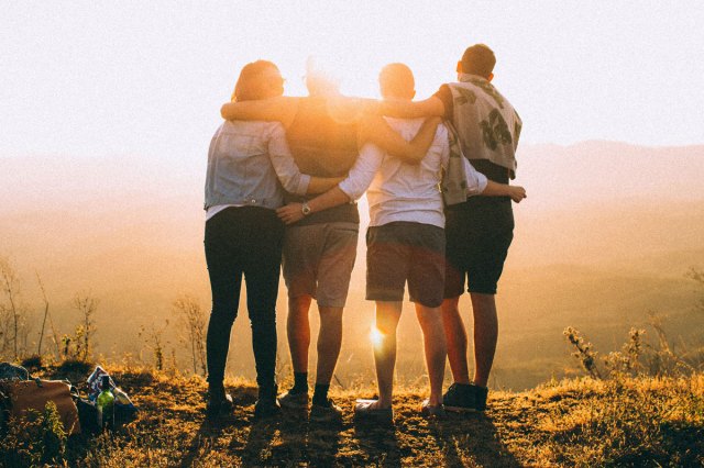 An image of four people with their arms around each other, looking at the sunset