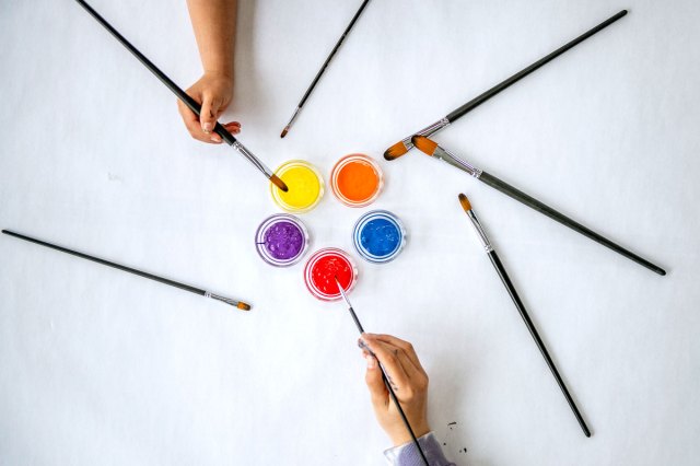 An image of paint brushes being dipped into various colors of paint