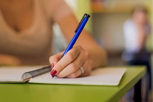 A close-up image of a girl writing something in a notebook with a blue pen