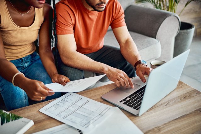 An image of a woman and a man sitting on a grey couch with paperwork and a laptop on a coffee table in front of them