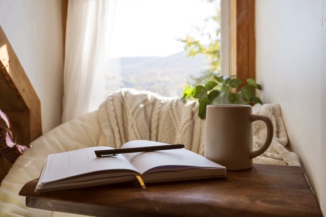 An image of an open book, a white coffee mug, and a white blanket near a window