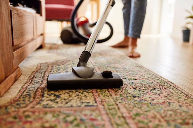 An image of a person vacuuming an oriental rug