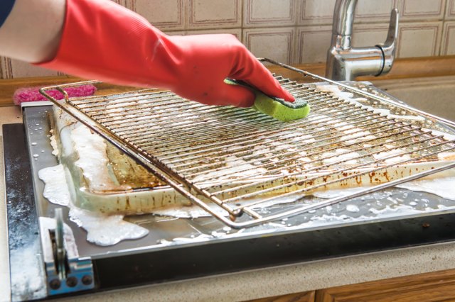 An image of a person scrubbing a dirty oven rack with a green sponge