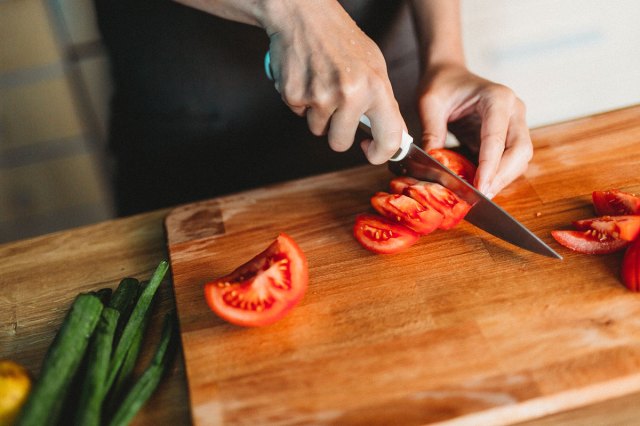 An image of a person slicing tomatoes on a wooden cutting board