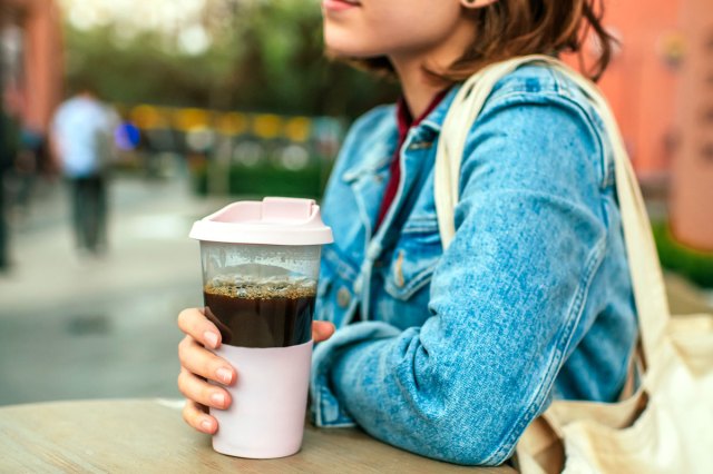 An image of a woman sitting at a table and holding an iced coffee