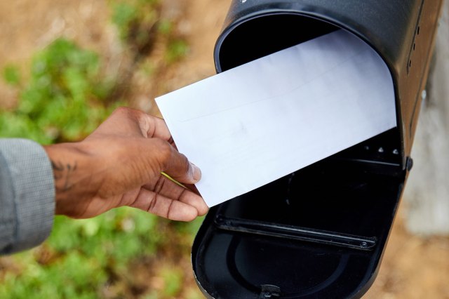An image of a hand putting a letter into a black mailbox