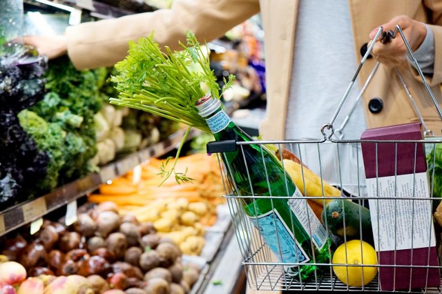 An image of a woman holding a basket with groceries, picking out produce