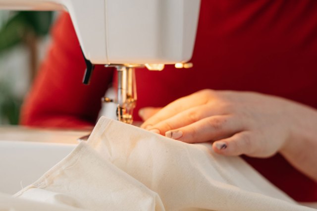 An image of a woman running fabric through a sewing machine