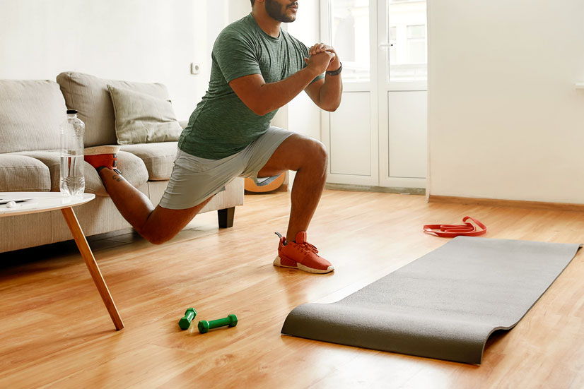 An image of a man exercising in front of a couch with a mat and weights on the floor
