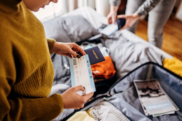 An image of a woman holding a plane ticket and passport while packing