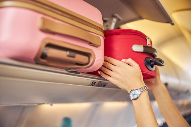 An image of a person putting a carry-on in a overhead storage bin