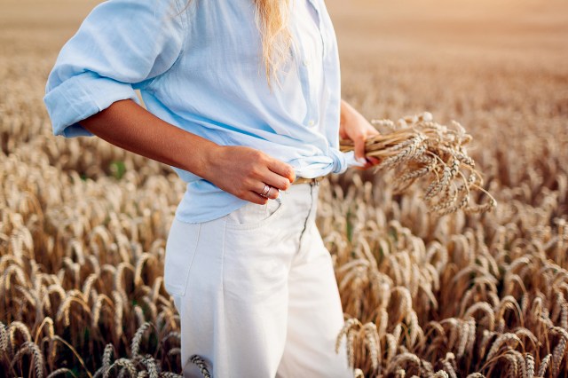 An image of a woman in a blue shirt and white pants in a wheat field