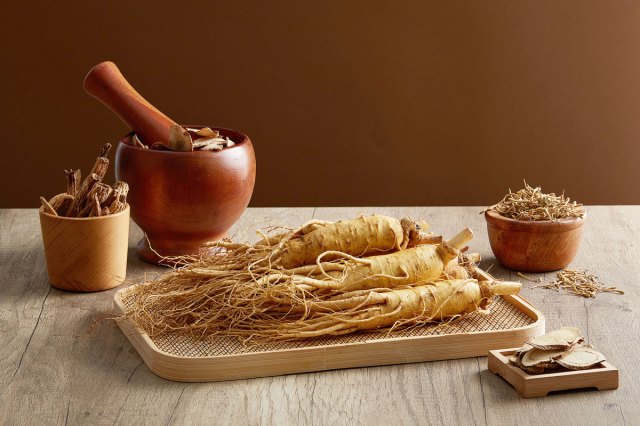 An image of ginseng roots and medicine herbs on wooden tray decorated with wooden mortar and pestle on brown background