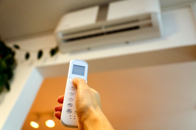 An image of a hand holding a remote and pointing it at a wall air conditioner