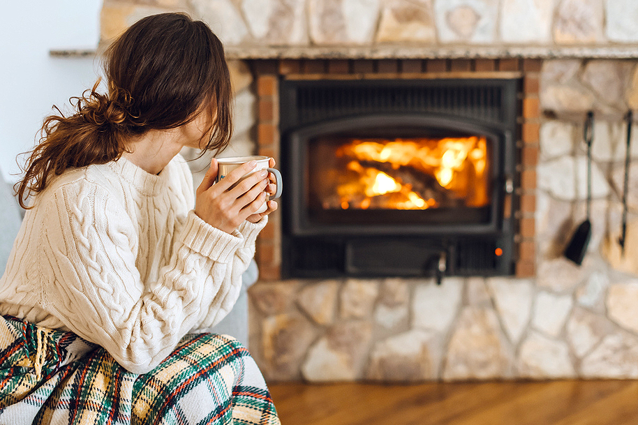 An image of a woman holding a coffee mug next to a fireplace 