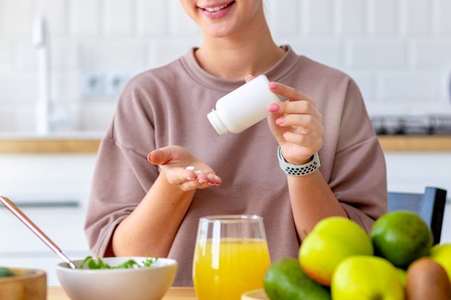 An image of a woman eating breakfast and taking vitamin sitting at home in the kitchen