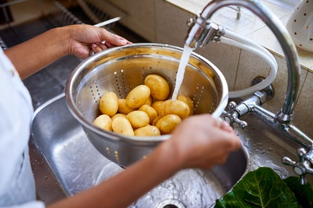 An image of a person washing potatoes in a colander in the sink