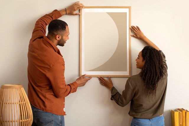 An image of a man and a woman hanging a piece of art on the wall