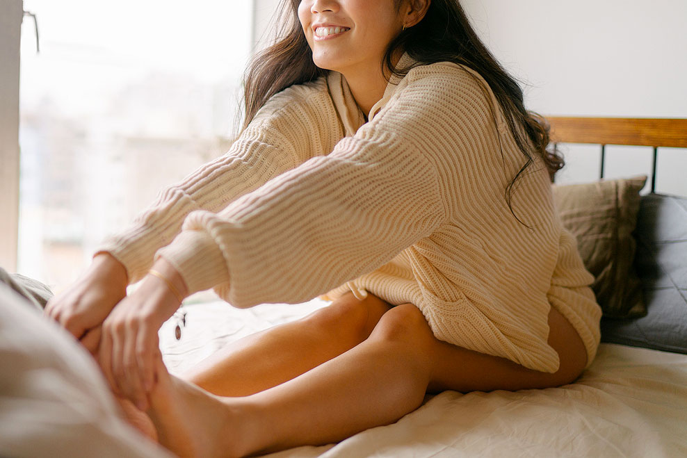 An image of a woman touching her toes while sitting on a bed