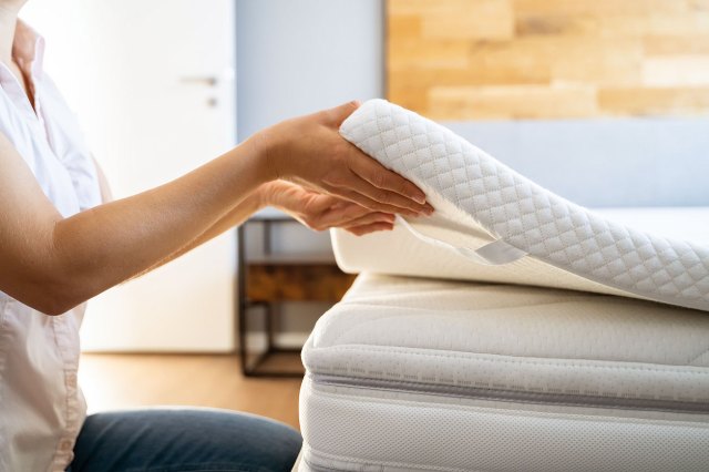 An image of a woman lifting a mattress pad off a bed