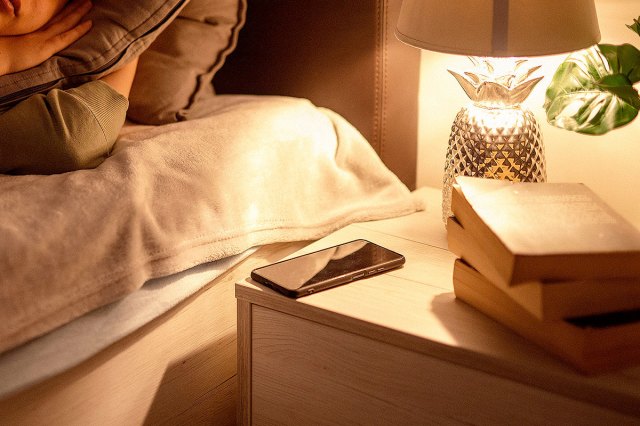 An image of a nightstand with a phone, a pineapple lamp, and a stack of books