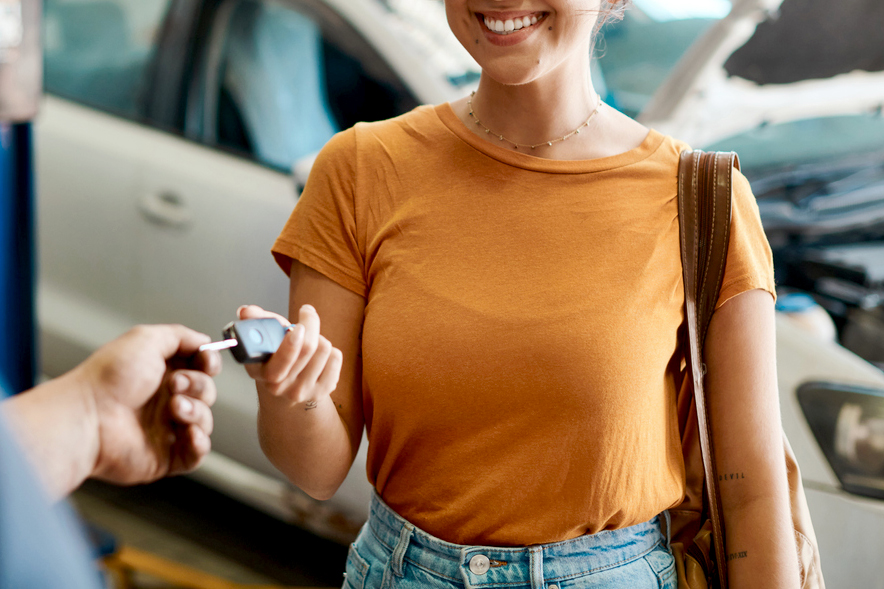 An image of a woman in an orange shirt handing over a car key