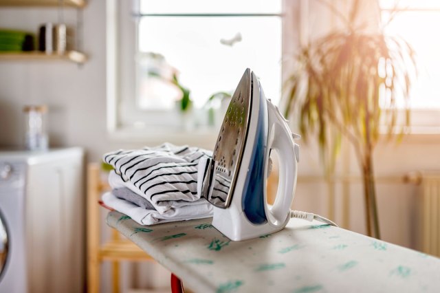 An image of an ironing board with an iron and folded shirts