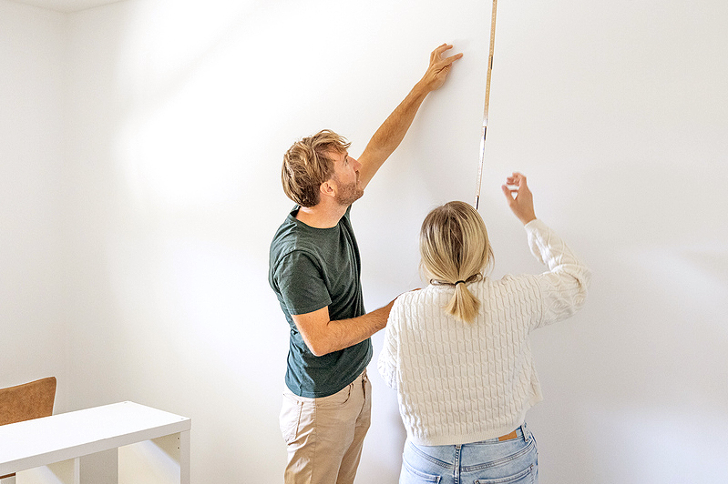 An image of a man and a woman measuring a wall