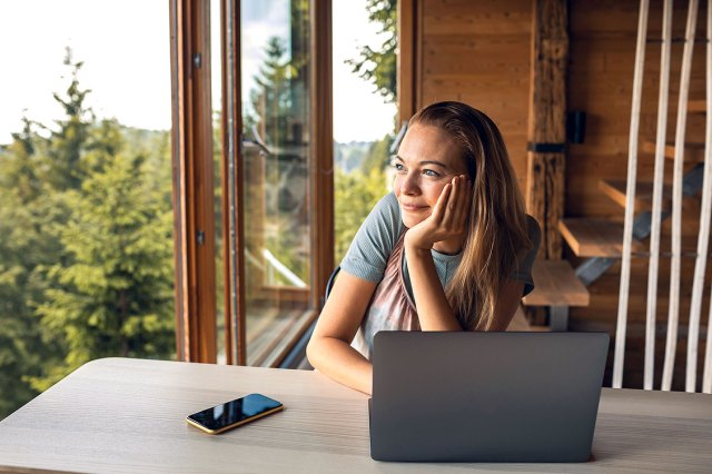 An image of a woman staring out a window with a laptop in front of her 