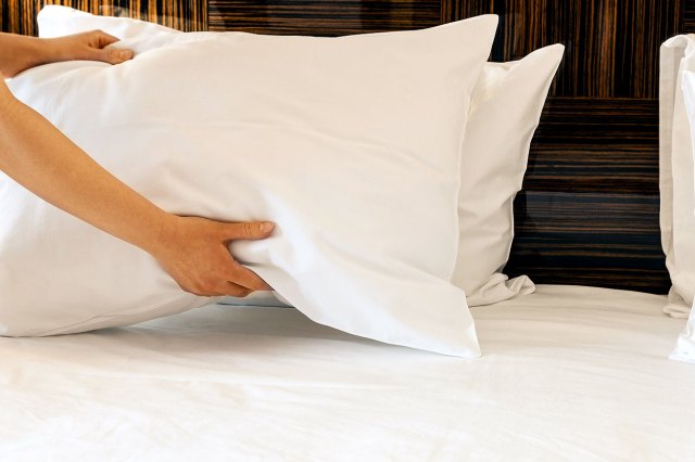 An image of hands putting a white pillow on a bed