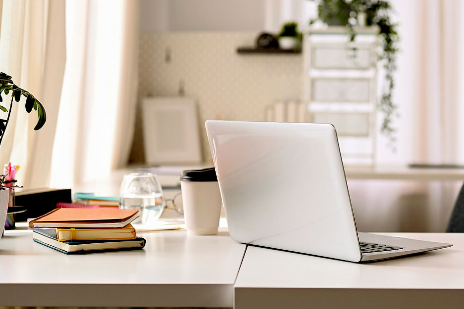 An image of a white desk with a laptop, books, and a coffee cup