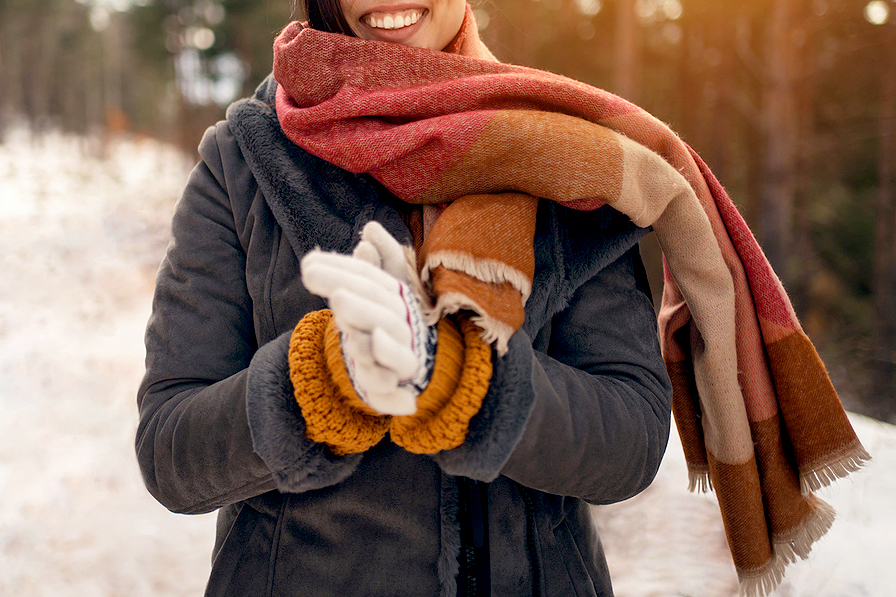 An image of a woman in a winter coat, scarf, and gloves